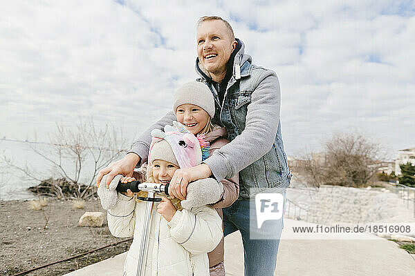Glücklicher Vater mit Töchtern  die auf einem Tretroller fahren