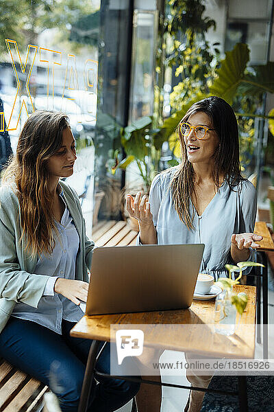 Businesswomen having discussion sitting with laptop in cafe