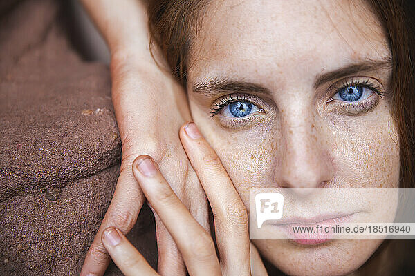 Junge Frau mit blauen Augen lehnt an Felsen