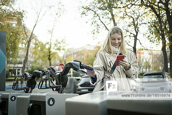 Woman using smart phone standing near bicycle at parking station