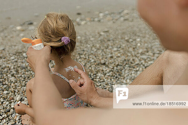 Man applying suntan lotion on daughter at beach