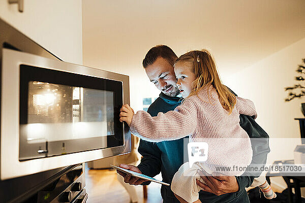 Father carrying daughter opening oven door in kitchen at home