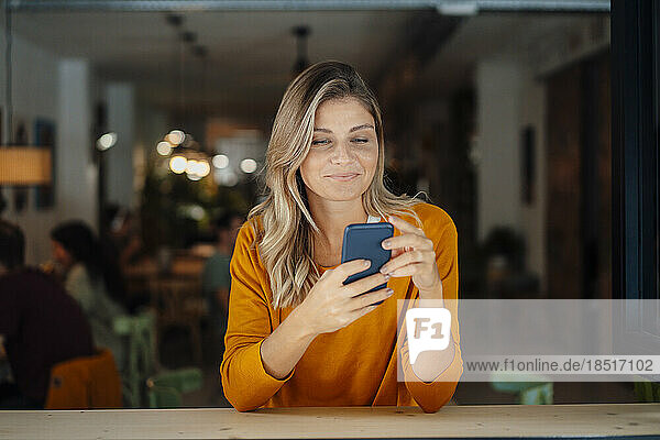 Lächelnde Frau mit Zopfhaar benutzt Smartphone im Café