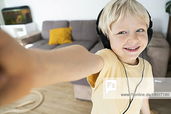Smiling blond boy wearing headphones taking selfie at home