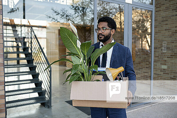 Thoughtful businessman carrying cardboard box leaving office building