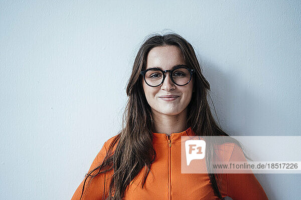 Smiling woman wearing eyeglasses leaning on white wall