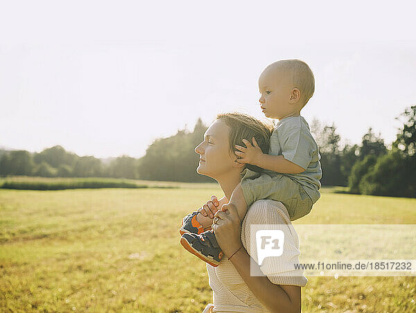Mother carrying son on shoulders in nature on sunny day