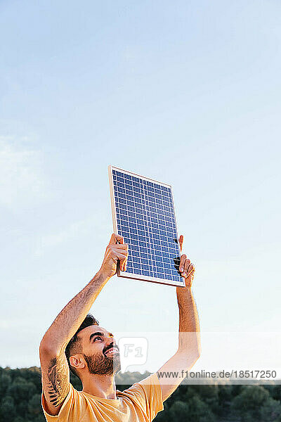 Lächelnder Mann  der an einem sonnigen Tag ein Solarpanel anhebt