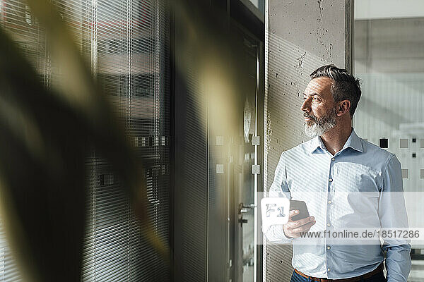 Geschäftsmann steht mit Smartphone im Büro