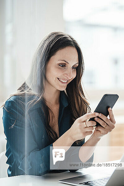 Happy young businesswoman using smart phone at home office