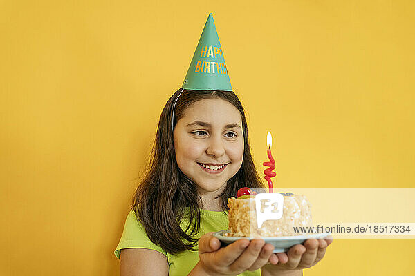 Smiling girl holding birthday cake against yellow background