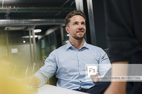 Smiling young businessman gesturing to colleague in office