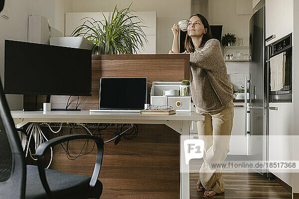 Thoughtful freelancer with coffee cup standing in home office
