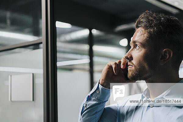 Thoughtful young businessman talking on smart phone in office