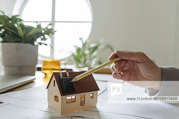 Hand of real estate agent with model house pointing pencil on solar panel