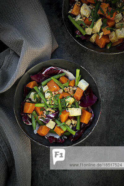 Two bowls of ready-to-eat vegetarian salad with sweet potato  celery  radicchio  green beans  croutons  walnuts and parsley