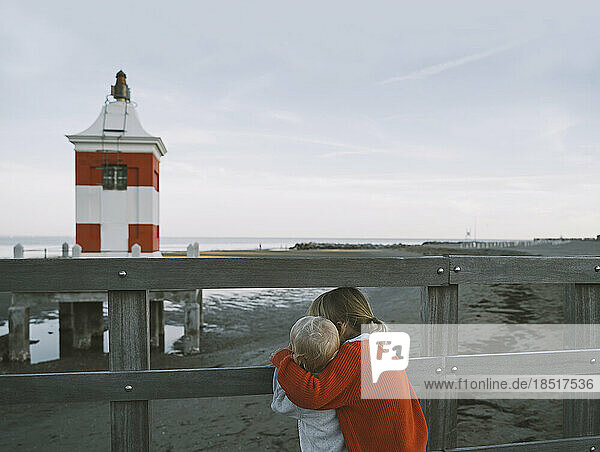 Brother and sister looking at lighthouse on shore