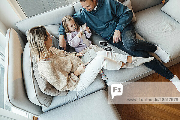 Daughter looking at ultrasound photos sitting by parents in living room