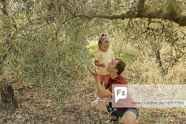 Smiling father showing olives to daughter in garden