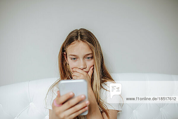 Worried girl using smart phone sitting on bed at home