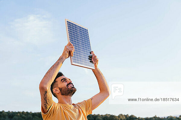 Lächelnder Mann hält Solarpanel an einem sonnigen Tag