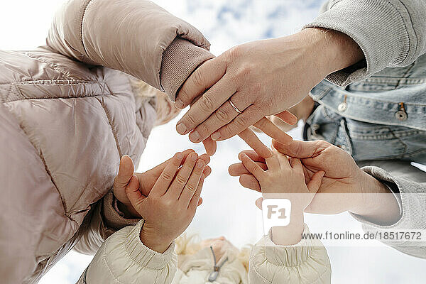 Father and daughters stacking hands together under sky