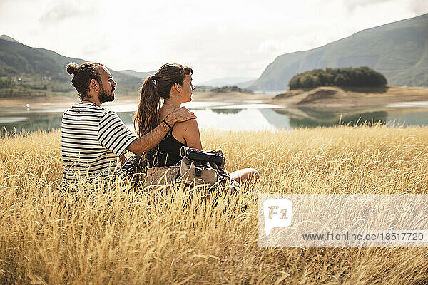Man sitting with arm around girlfriend on dry grass