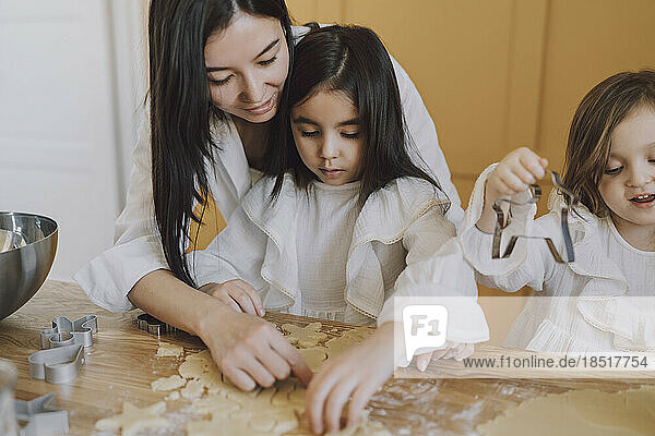 Mother helping daughters in making cookies for Easter