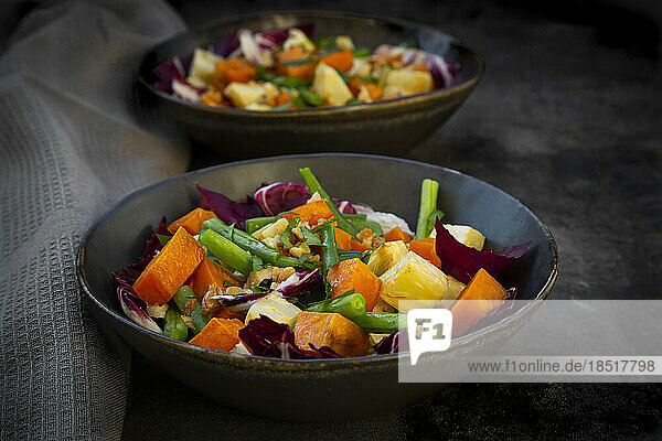 Two bowls of ready-to-eat vegetarian salad with sweet potato  celery  radicchio  green beans  croutons  walnuts and parsley