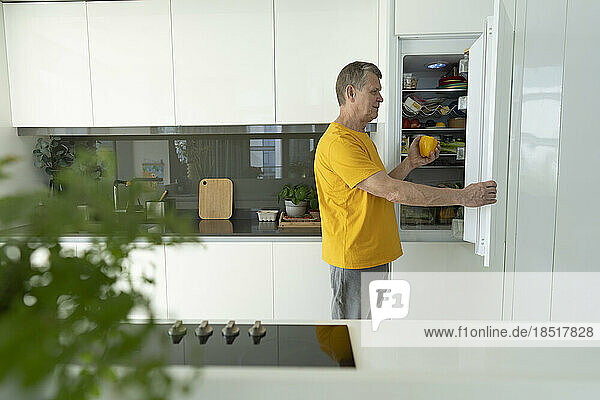 Senior man opening refrigerator door in kitchen at home