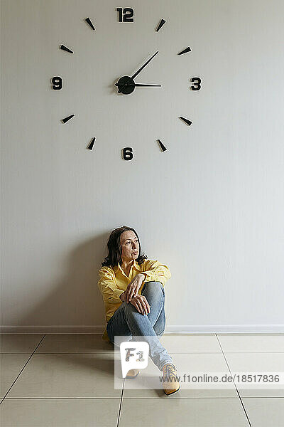 Nachdenkliche Frau sitzt unter der Uhr auf dem Boden