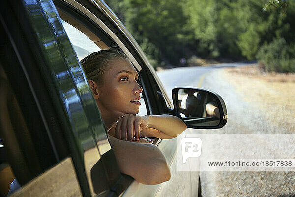 Nachdenkliche junge Frau lehnt am Autofenster