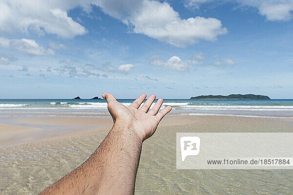 Die Hand des Mannes greift am Strand in Richtung Meer