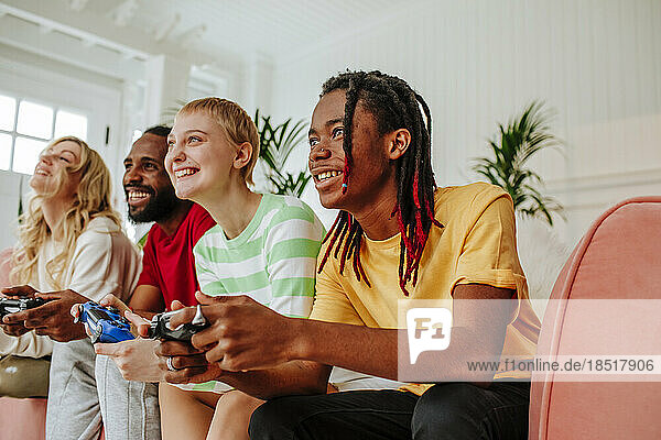 Smiling young man with dreadlocks playing video game by friends at home