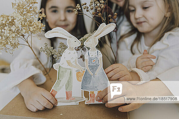 Mother and daughters holding paper Easter bunnies at home