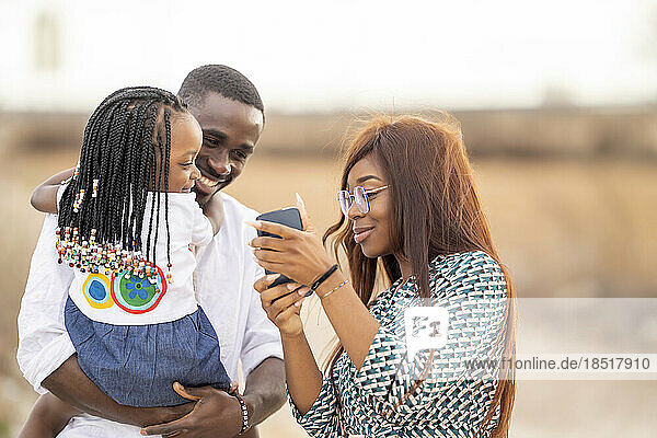 Smiling woman showing smart phone to man and daughter