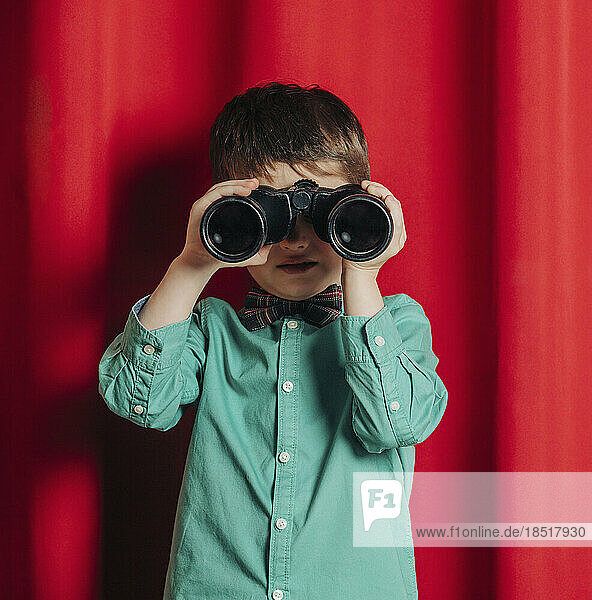 Boy looking through binoculars in front of curtain