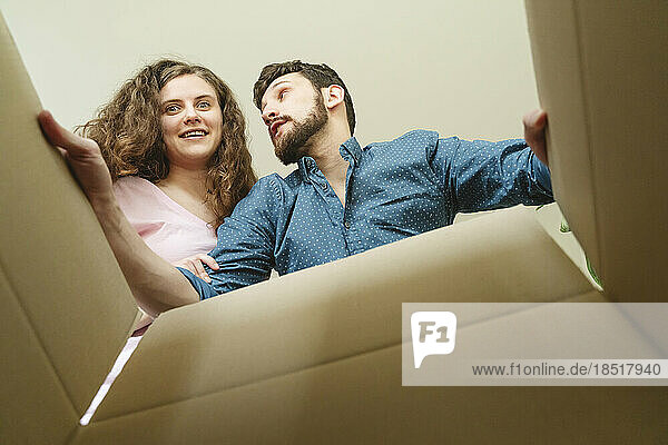 Glückliches junges Paar öffnet Karton im neuen Zuhause
