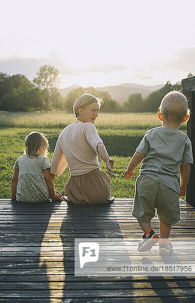 Mother sitting with daughter and son walking on wooden footbridge