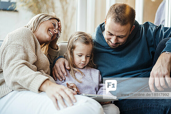 Father looking at girl using tablet PC by mother at home