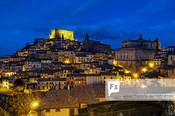Illuminated Castello Orsini over houses under blue sky at night