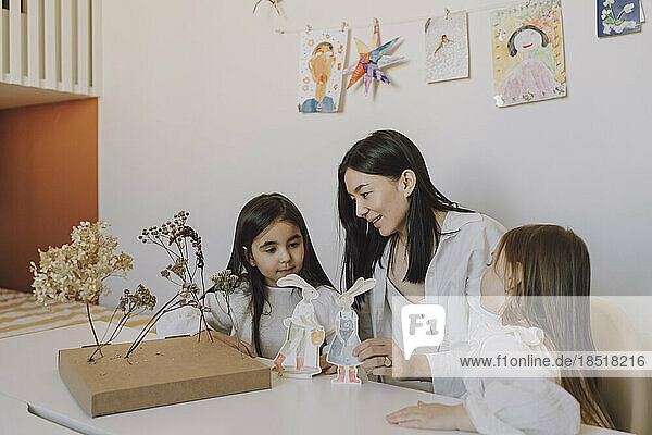 Mother and daughters playing with paper Easter bunnies at home