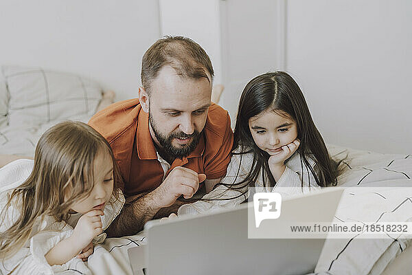 Vater und Töchter schauen auf den Laptop im Bett