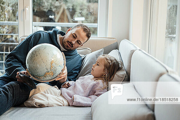 Father showing globe to daughter sitting on sofa in living room