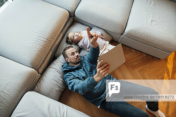 Vater hält Tablet-PC in der Hand und gestikuliert mit Tochter  die zu Hause liegt