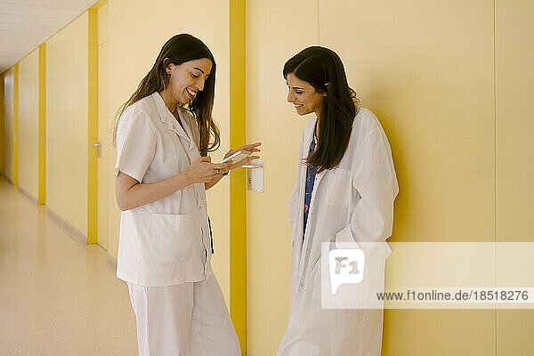 Smiling doctors sharing smart phone standing in corridor