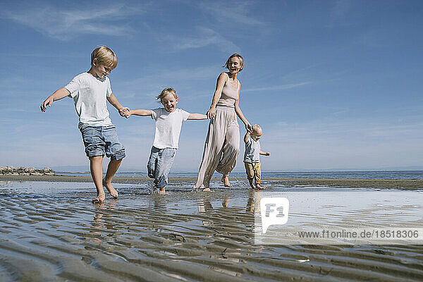 Happy mother holding hands with children and enjoying at beach