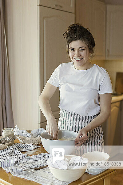 Happy young woman mixing bread dough at home