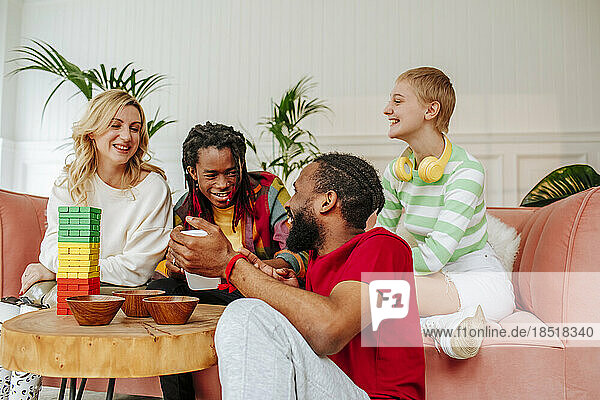 Young man sharing mobile phone with friends playing toy block game at home