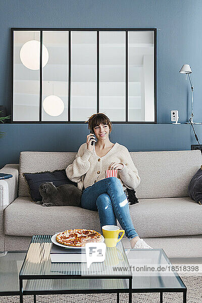 Smiling woman talking through smart phone sitting on sofa at home